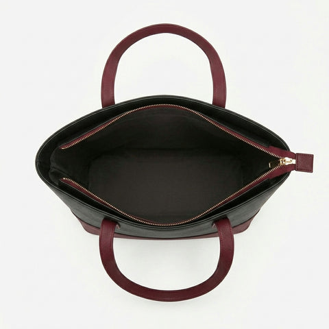 Black and maroon tote bag with maroon handles and zipper on a white background